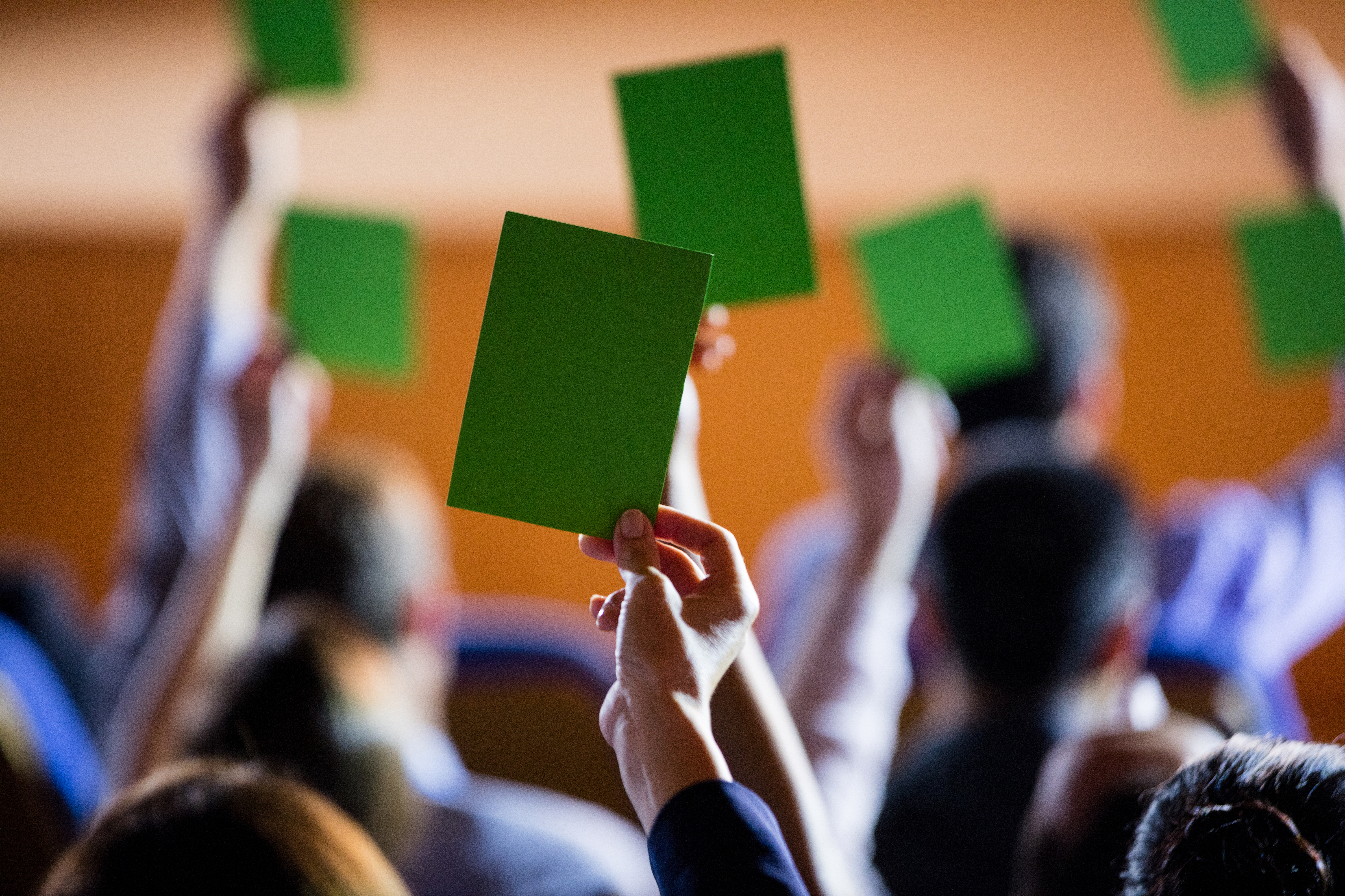 Rear view of business executives show their approval by raising hands at conference center